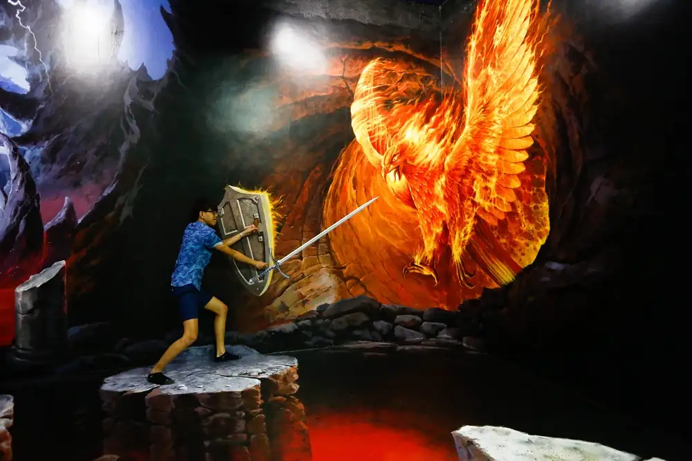 Visitor posing with a sword and shield in front of a fiery phoenix artwork (Source: Art in Paradise Da Nang)