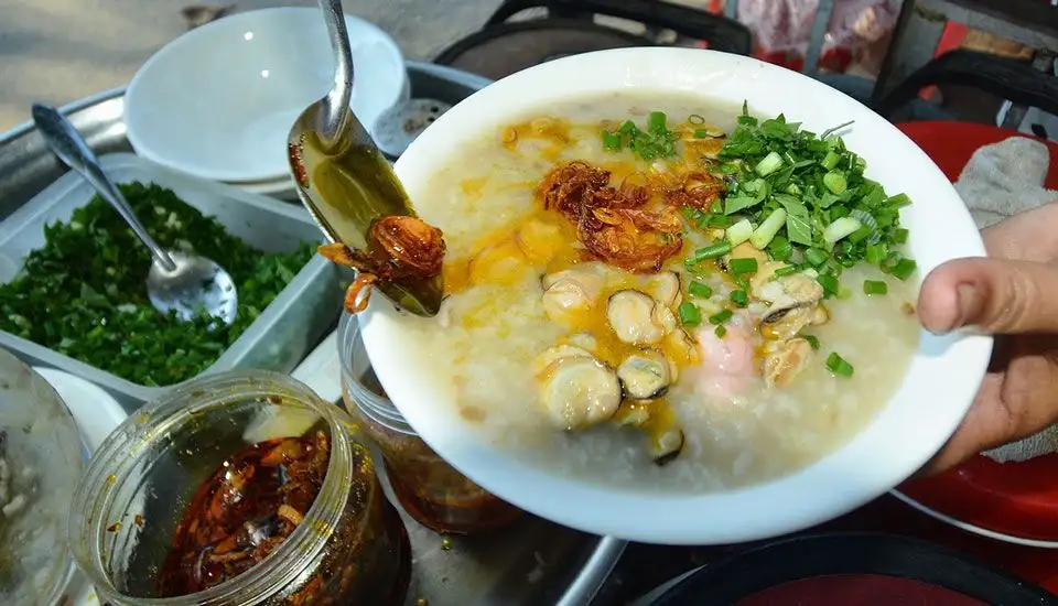 A steaming bowl of Hoi An clam porridge topped with sautéed clams, crispy shallots, and fresh herbs (Source: Trung tam van hoa Hoi An)