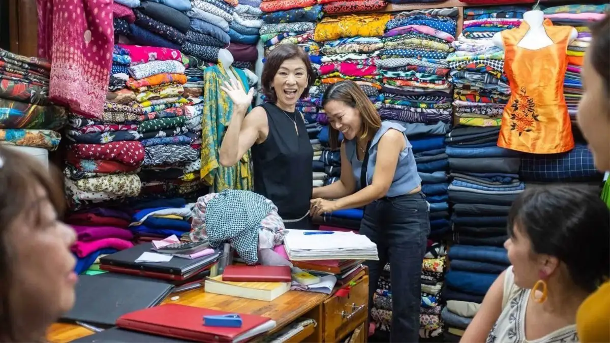 Hoi An tailor shop with colorful fabrics and a tailor measuring a customer (Source: eva.vn)