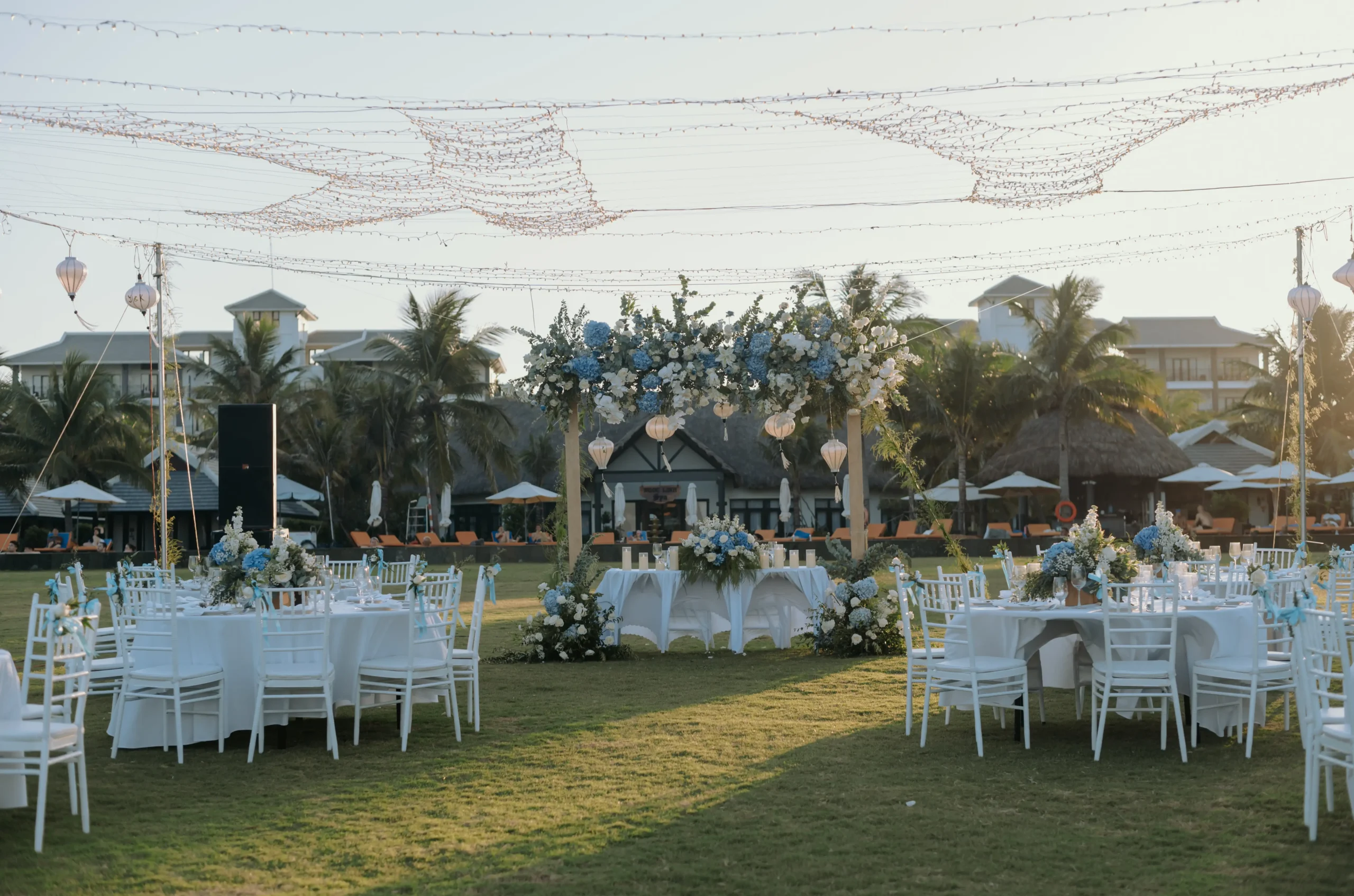 Reception tables with blue and white flowers, lanterns and fairy lights on the lawn
