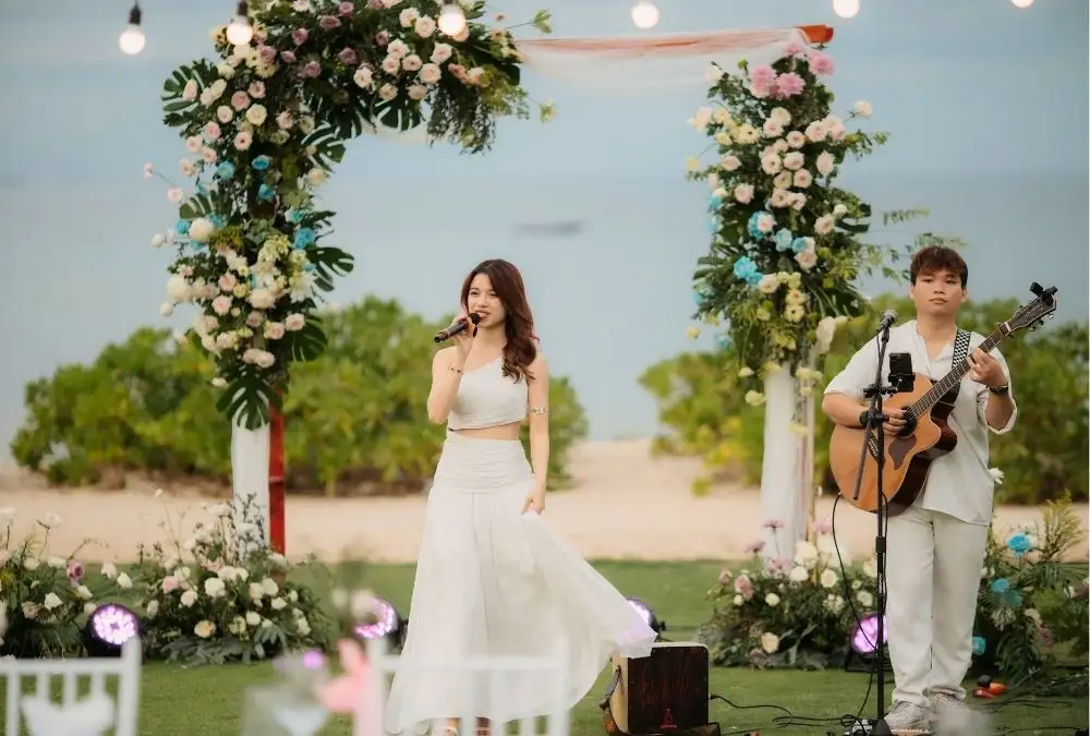 A singer and a guitarist perform beside the floral arch as evening settles in